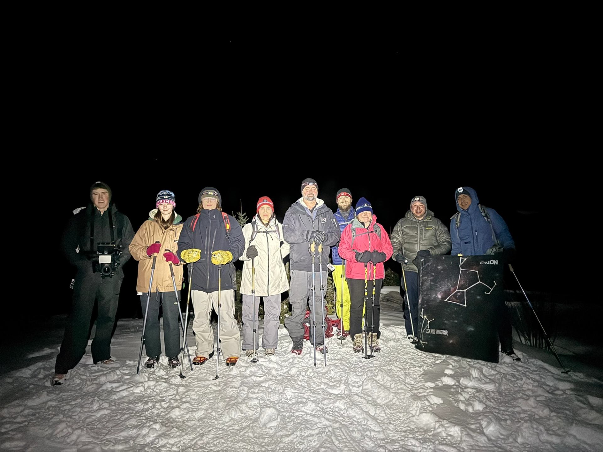 Group stands on snowy ground at night during guided snowshoe outing.