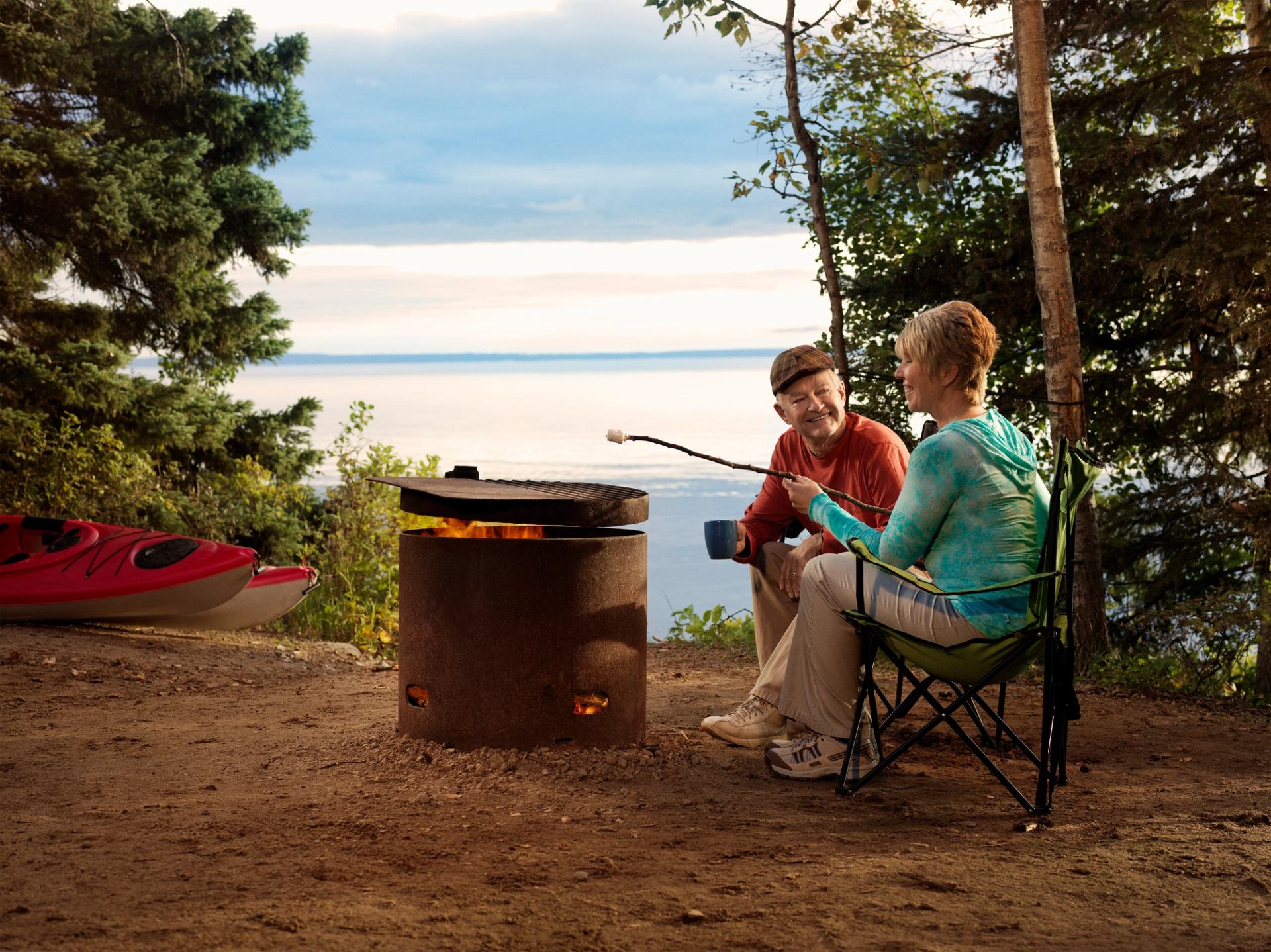 Older couple roasting marshmallows by a campfire while camping at Cold in Lake Northern Alberta.