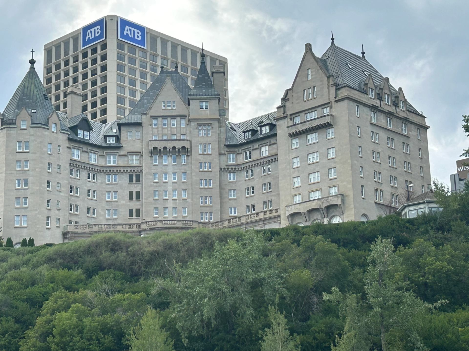 Historic turreted building on hill with modern high-rise in background and greenery below.