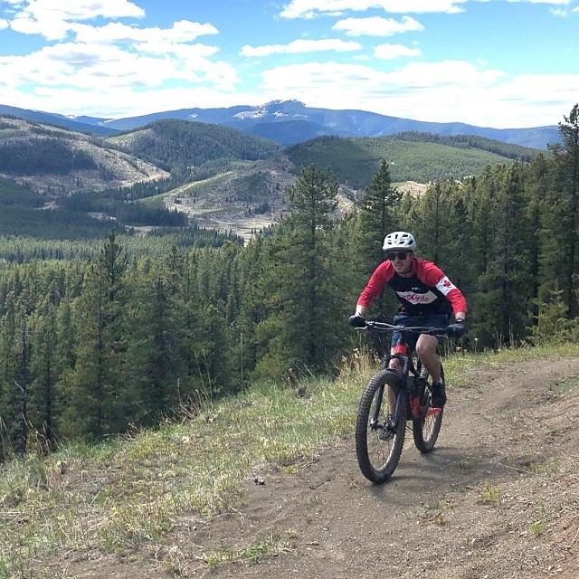Mountain biker on dirt trail above forested hills and distant mountains.