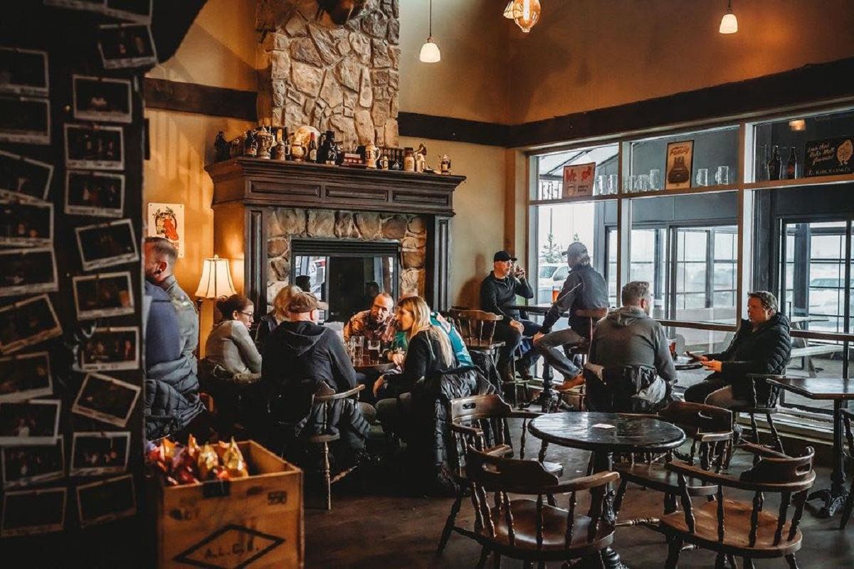Brewpub interior with people seated at tables near a stone fireplace and glass storefront.