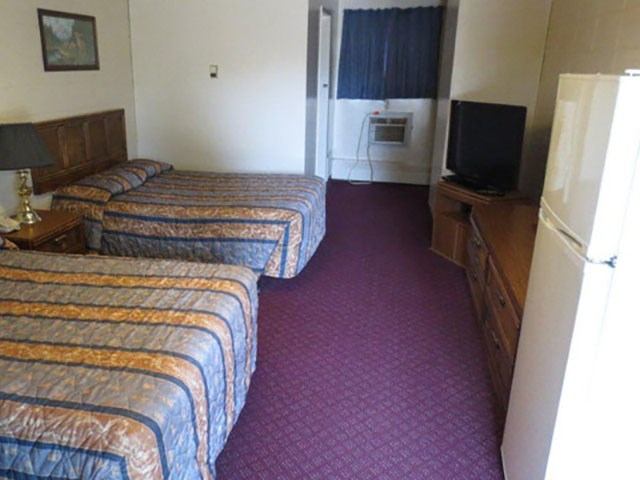 Motel room with two double beds, TV, dresser, mini-fridge, and purple carpet.