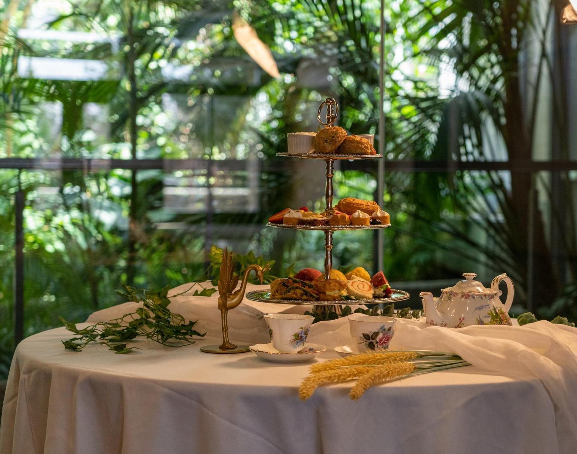 Two-tier tea stand with pastries on a table, with garden greenery in background.