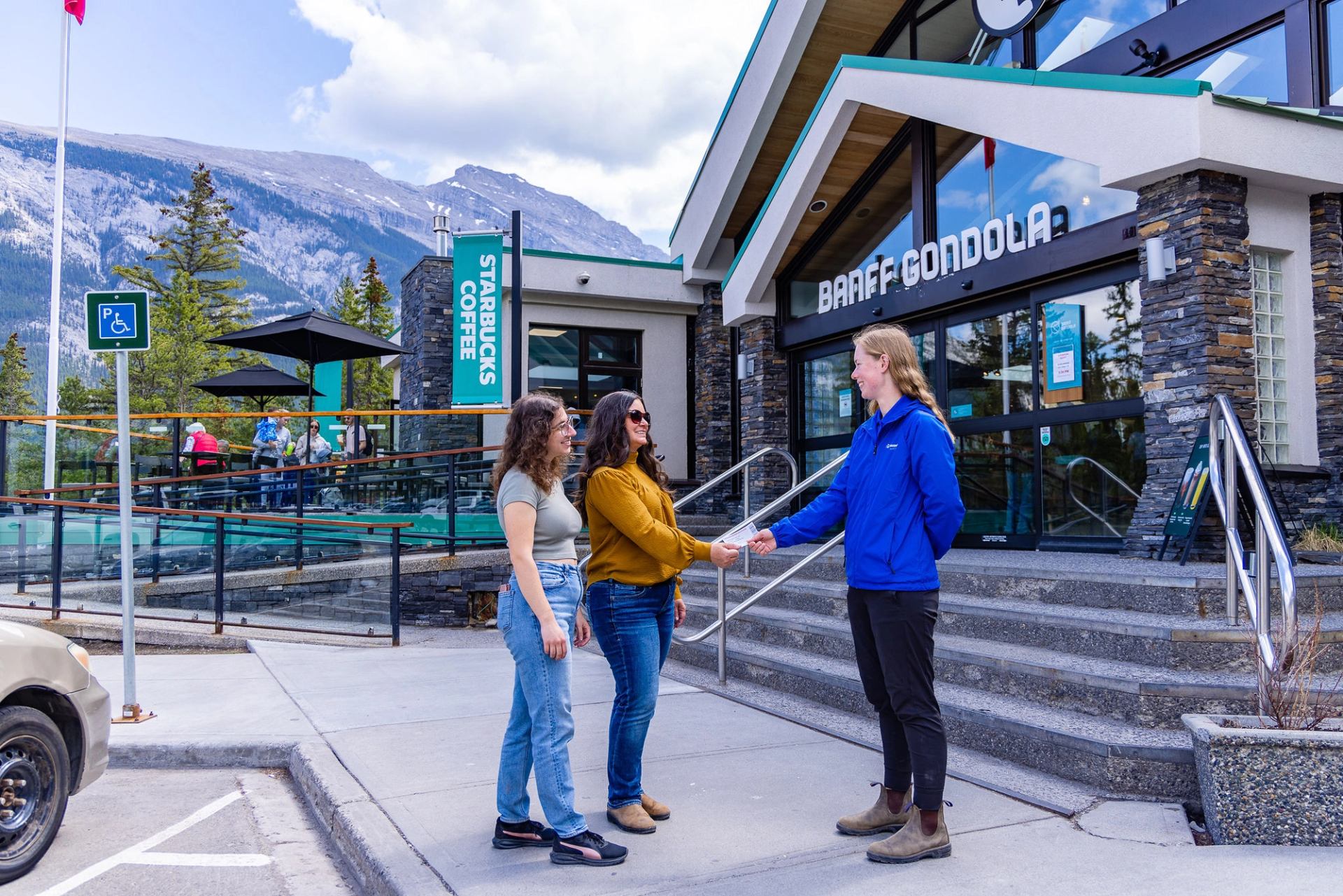 Three people stand outside Banff Gondola entrance, shaking hands near Starbucks Coffee.