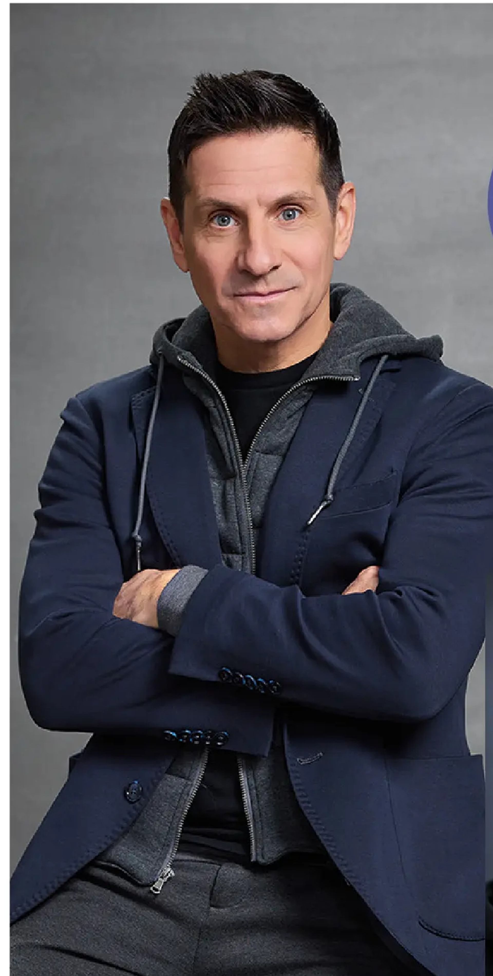 Person in a navy blazer and grey hoodie poses with arms crossed.