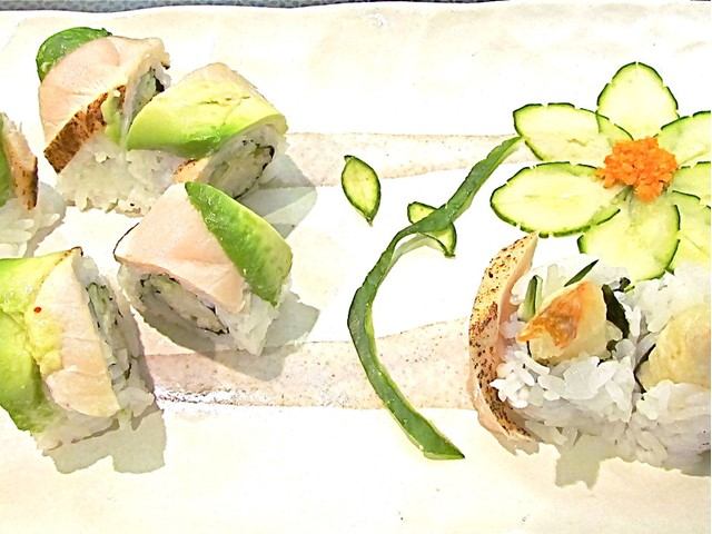 Assorted sushi rolls topped with avocado and arranged with a decorative cucumber flower.
