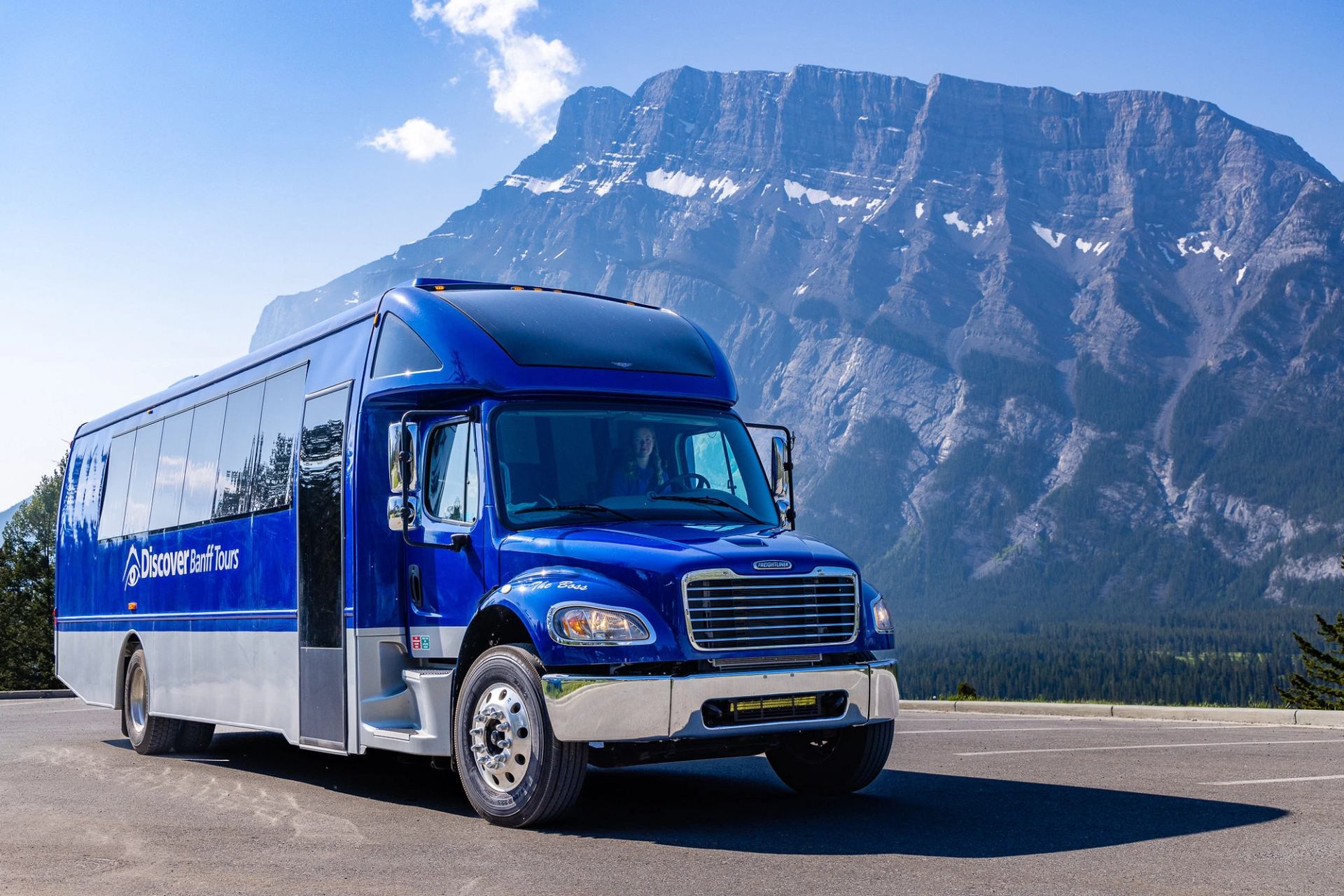 Blue Discover Banff Tours bus parked on roadside with large rocky mountain backdrop.