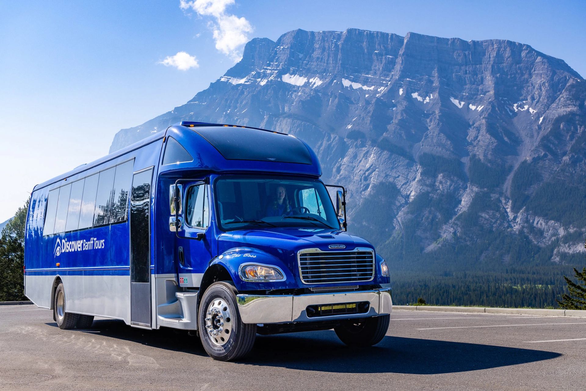 Blue Discover Banff Tours bus parked on roadside with large rocky mountain backdrop.