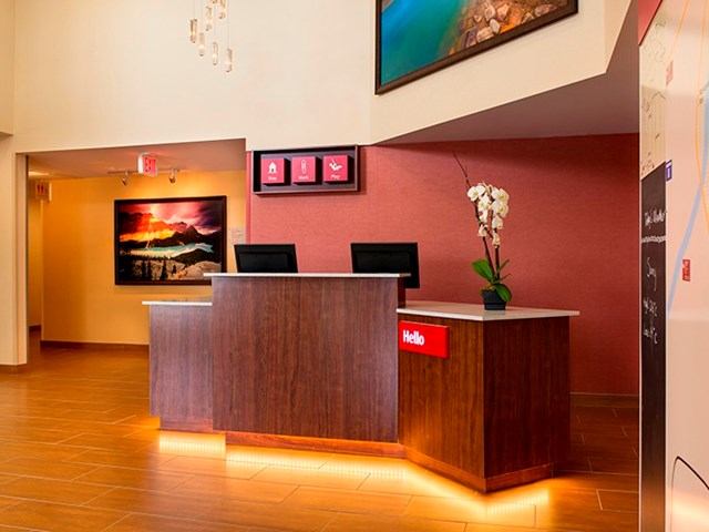 Hotel reception desk with red wall, framed art, orchid, and warm lighting.