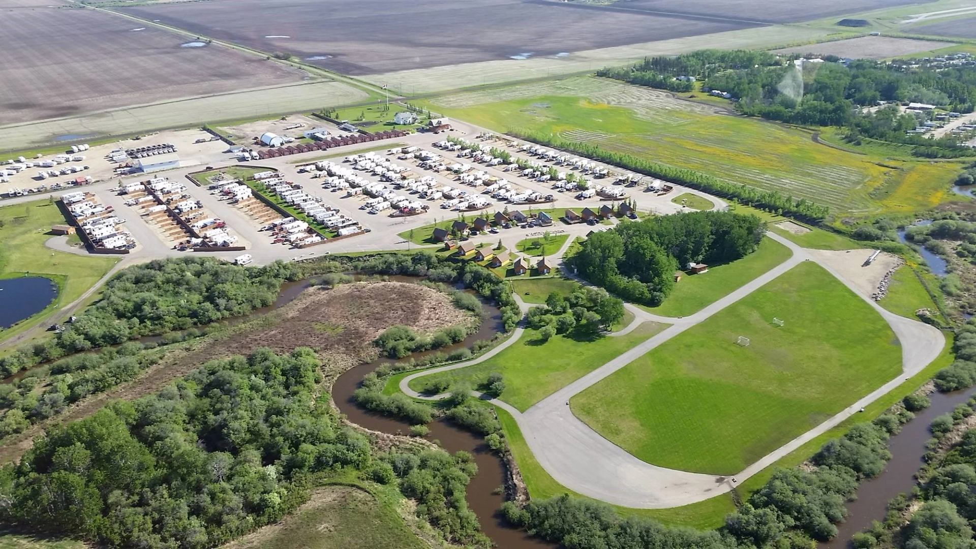 Aerial view of Happy Trails Campground with RV sites, cabins, and winding roads near a river.