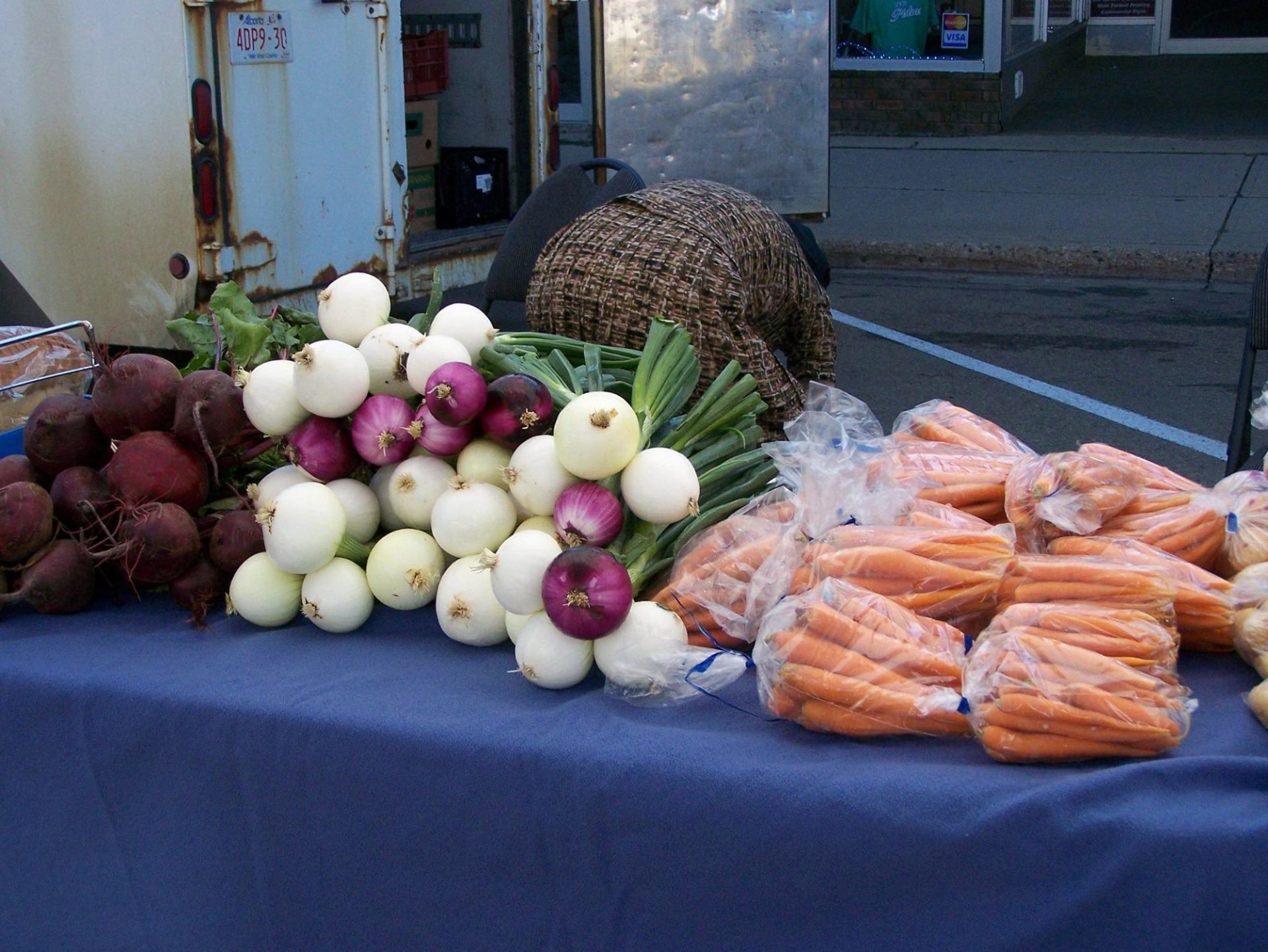 Table display of beets, onions, green onions, and bagged carrots beside a wicker basket.