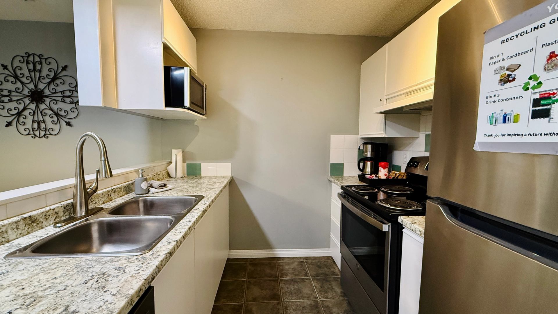 Galley kitchen with granite counters, double sink, white cabinets and stainless steel appliances.