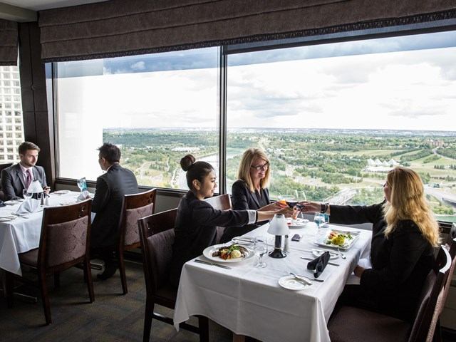 Hotel dining room with guests, white tablecloths, and scenic river views.