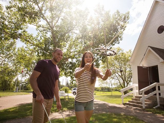 Two visitors playing a traditional outdoor game near a historic white building under sunny skies.