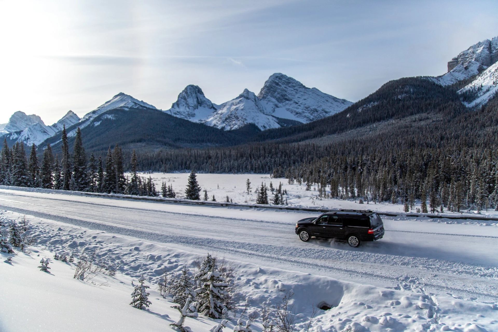 Black SUV driving on a snow-covered road with rugged mountain peaks in the background