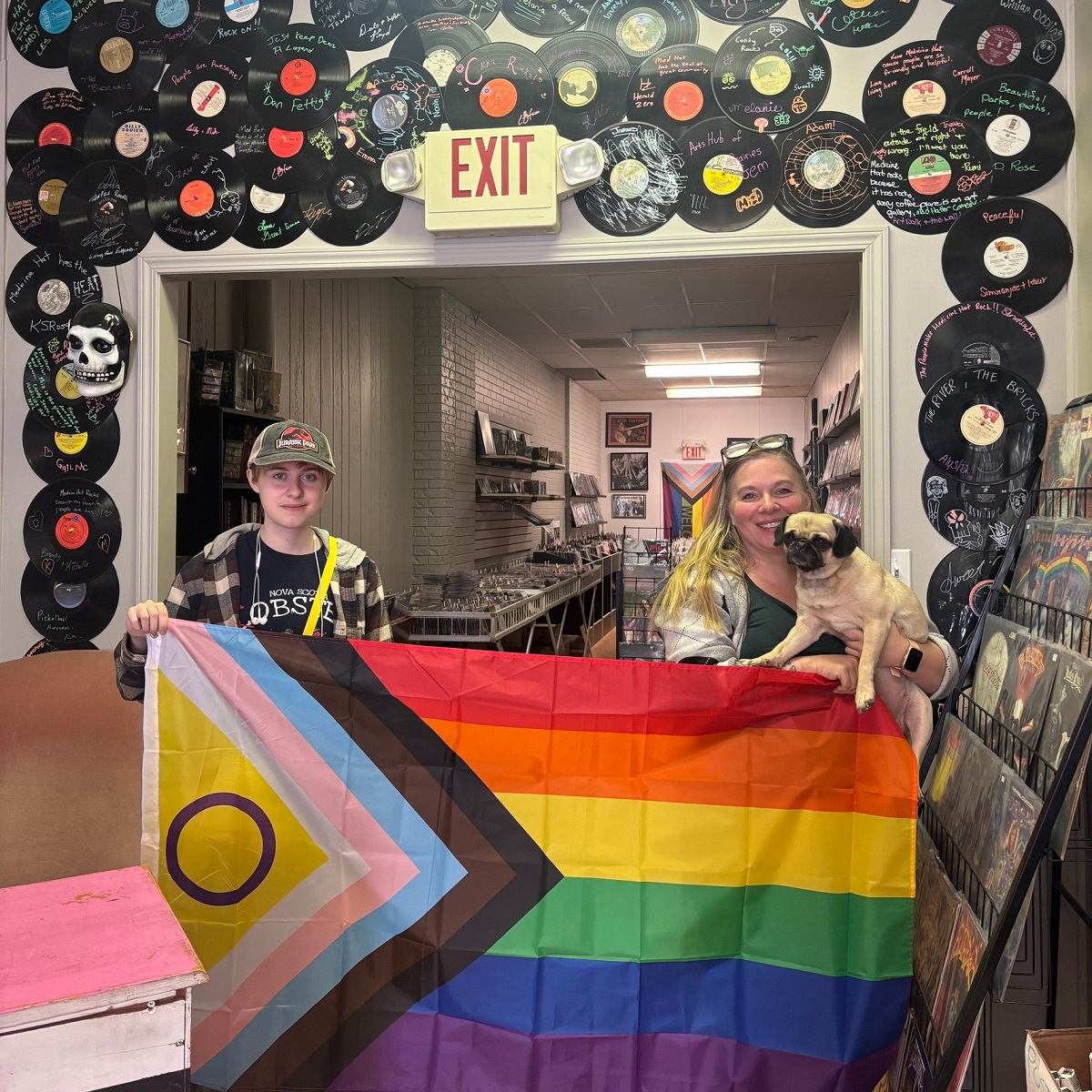 Two people holding a Pride flag inside a record shop decorated with vinyl records.