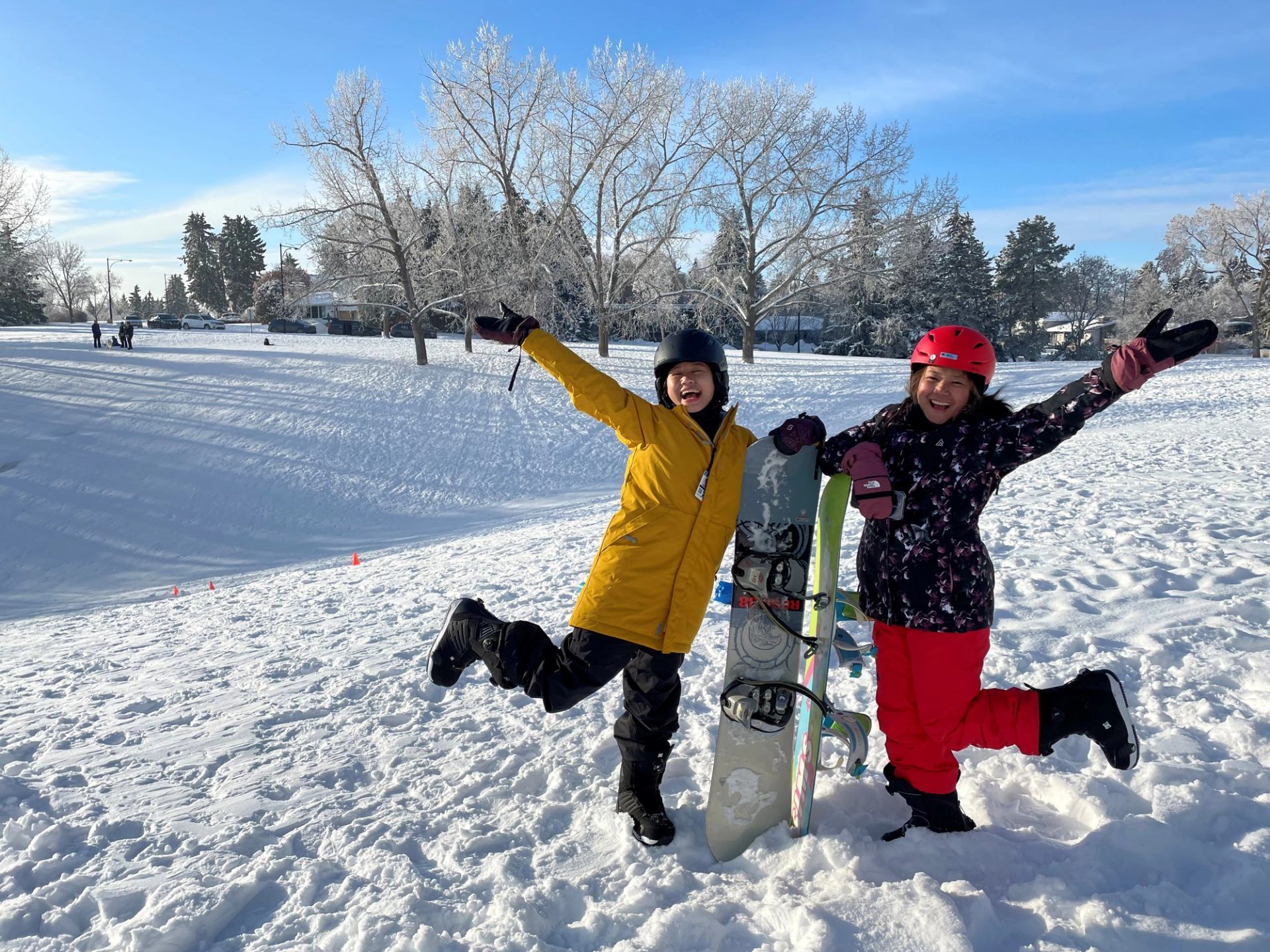 Snowboard riders in helmets standing on a snow-covered field with boards and boots.