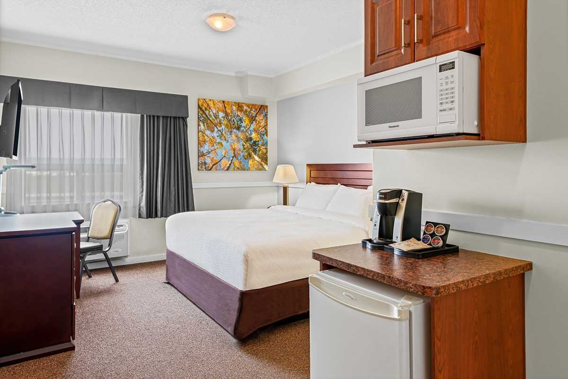 Hotel room with bed, desk, window, microwave, mini-fridge and coffee maker.