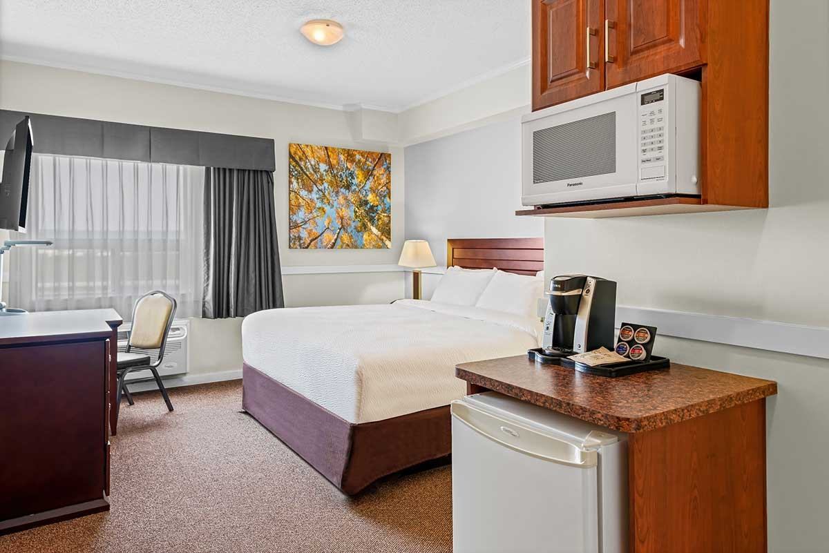 Hotel room with bed, desk, window, microwave, mini-fridge and coffee maker.
