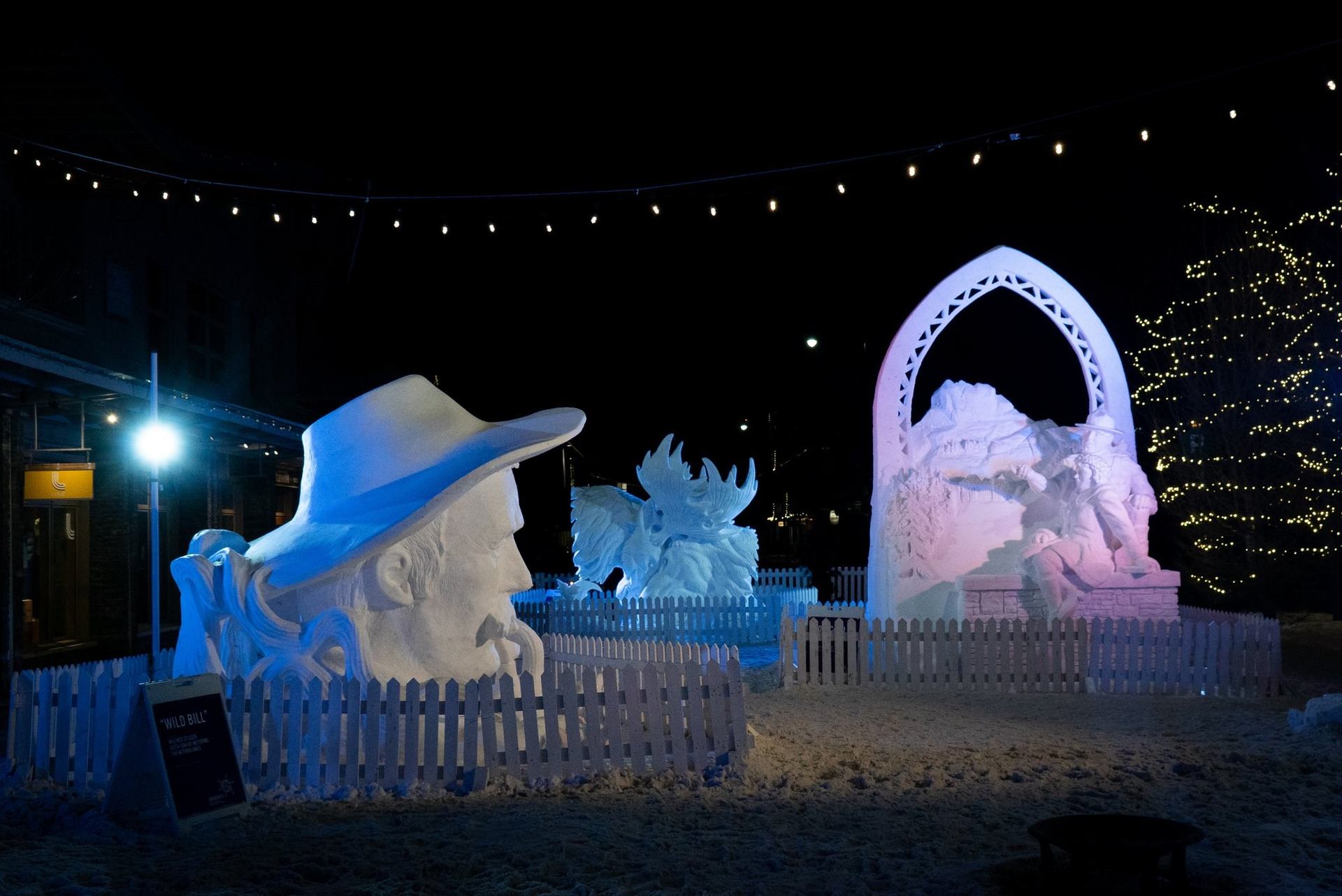 Illuminated snow sculptures at night, featuring figures and archways in a festive outdoor display.