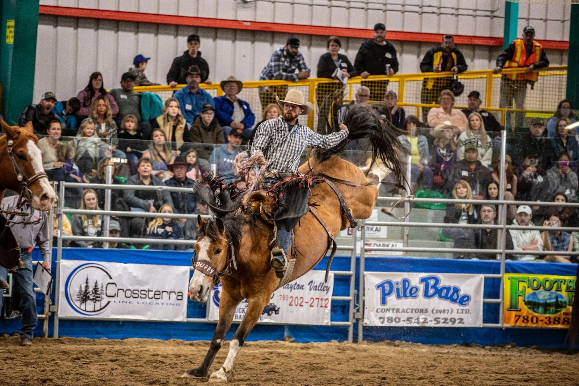 Bronc rider gripping tight as a bucking horse twists mid‑ride inside a packed indoor rodeo arena.