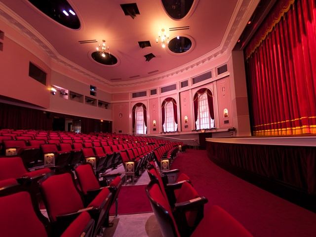 Red theatre interior with rows of seats, stage, and red curtains at Capitol Theatre.