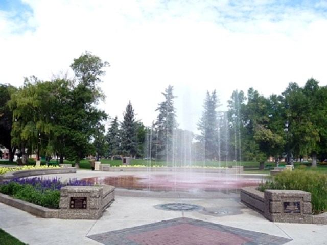 Fountain sprays in paved plaza with flower beds and trees.