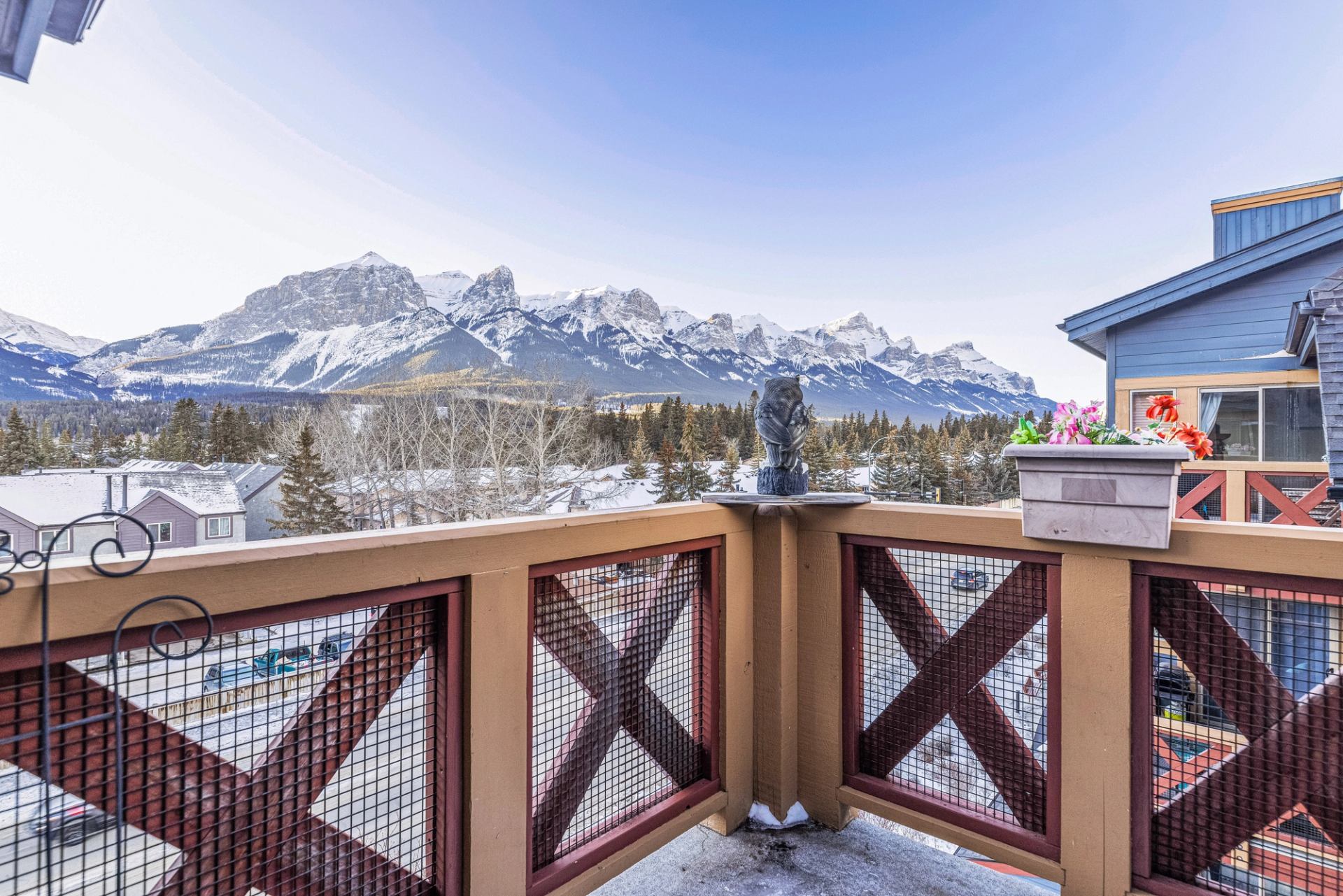 Balcony railing with owl statue and flowers overlooking snowy mountain range and town.