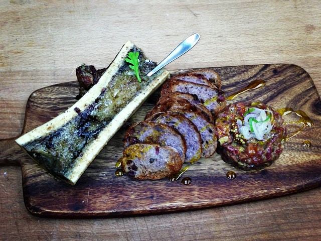 Gourmet trio: bone marrow, sliced meat, and tartare on a wooden board.