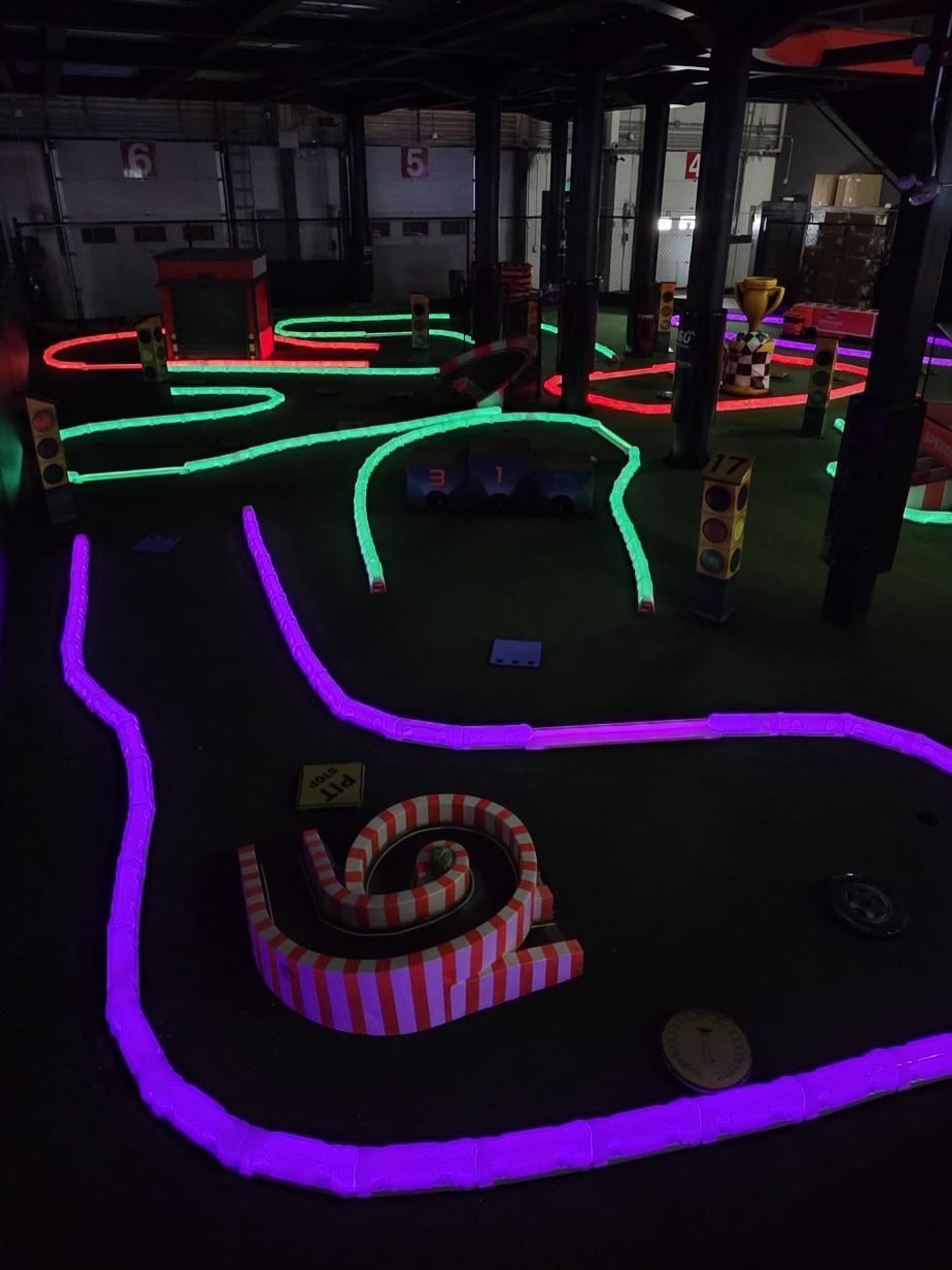 Indoor mini racetrack with glowing neon lanes, traffic lights and striped spiral obstacle.