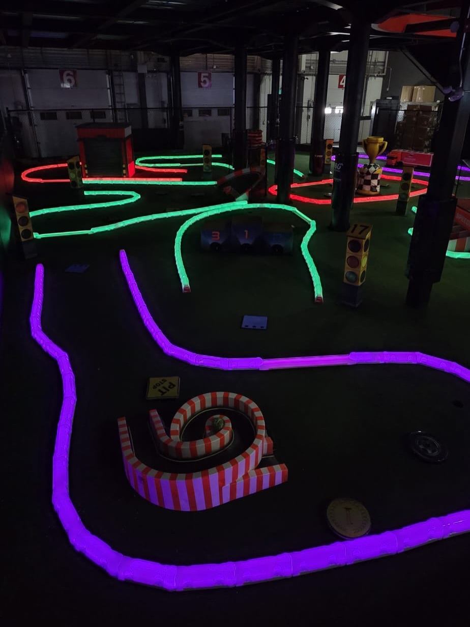 Indoor mini racetrack with glowing neon lanes, traffic lights and striped spiral obstacle.