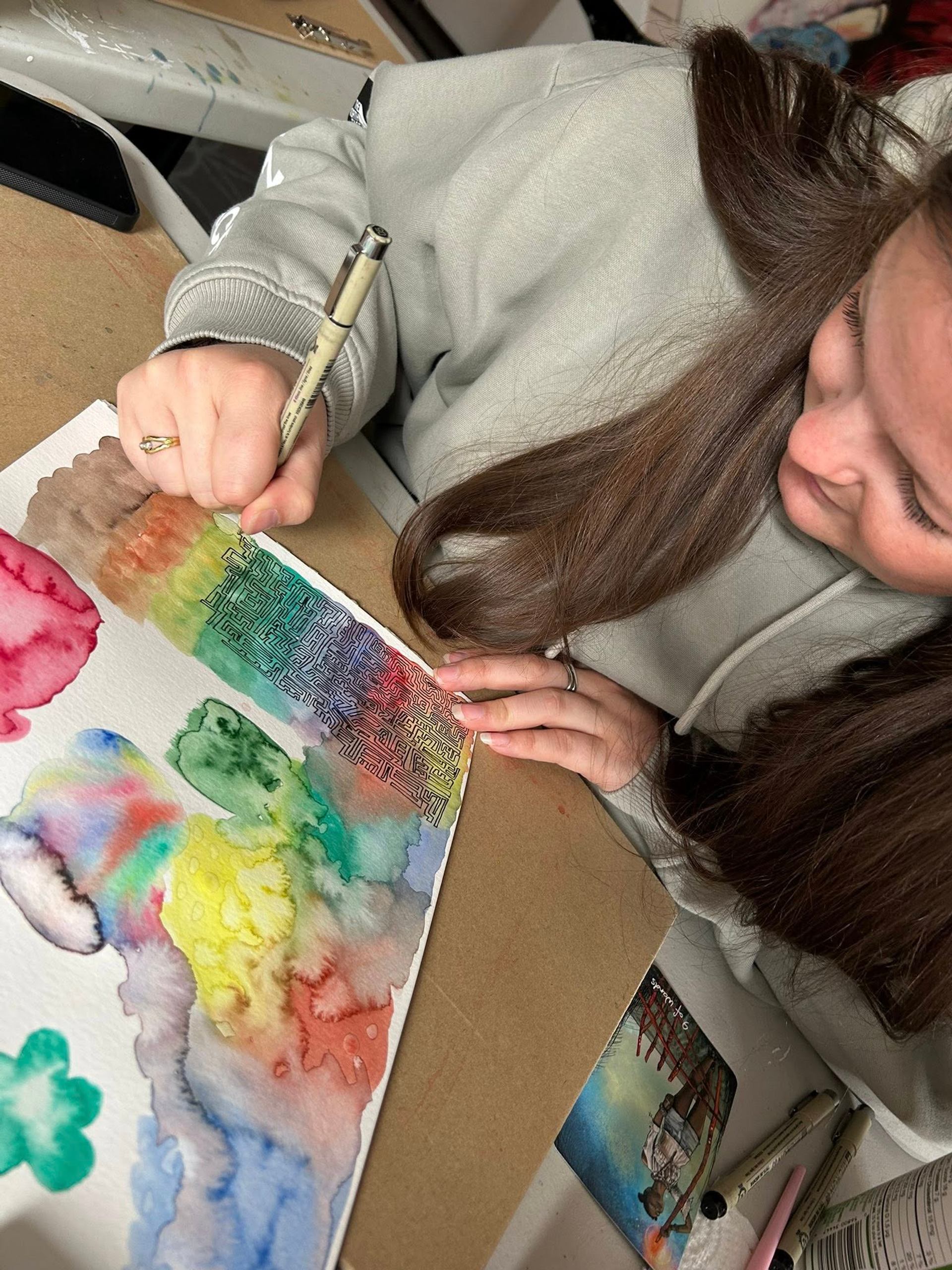 Person adding details to colorful watercolor painting.