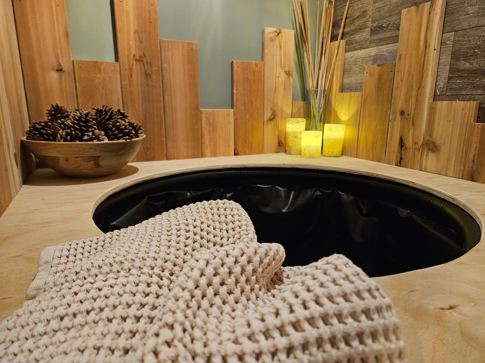Rustic spa setup with basin, towel, pinecones, and lit candles.