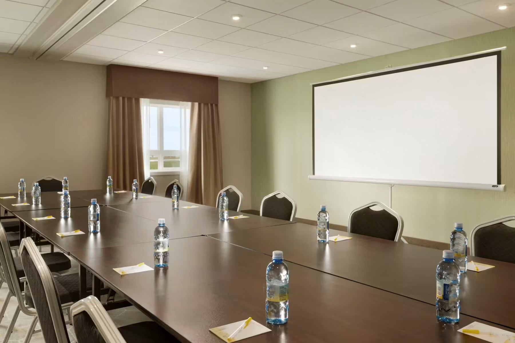 Conference room with long table, water bottles, chairs, and a blank projector screen.