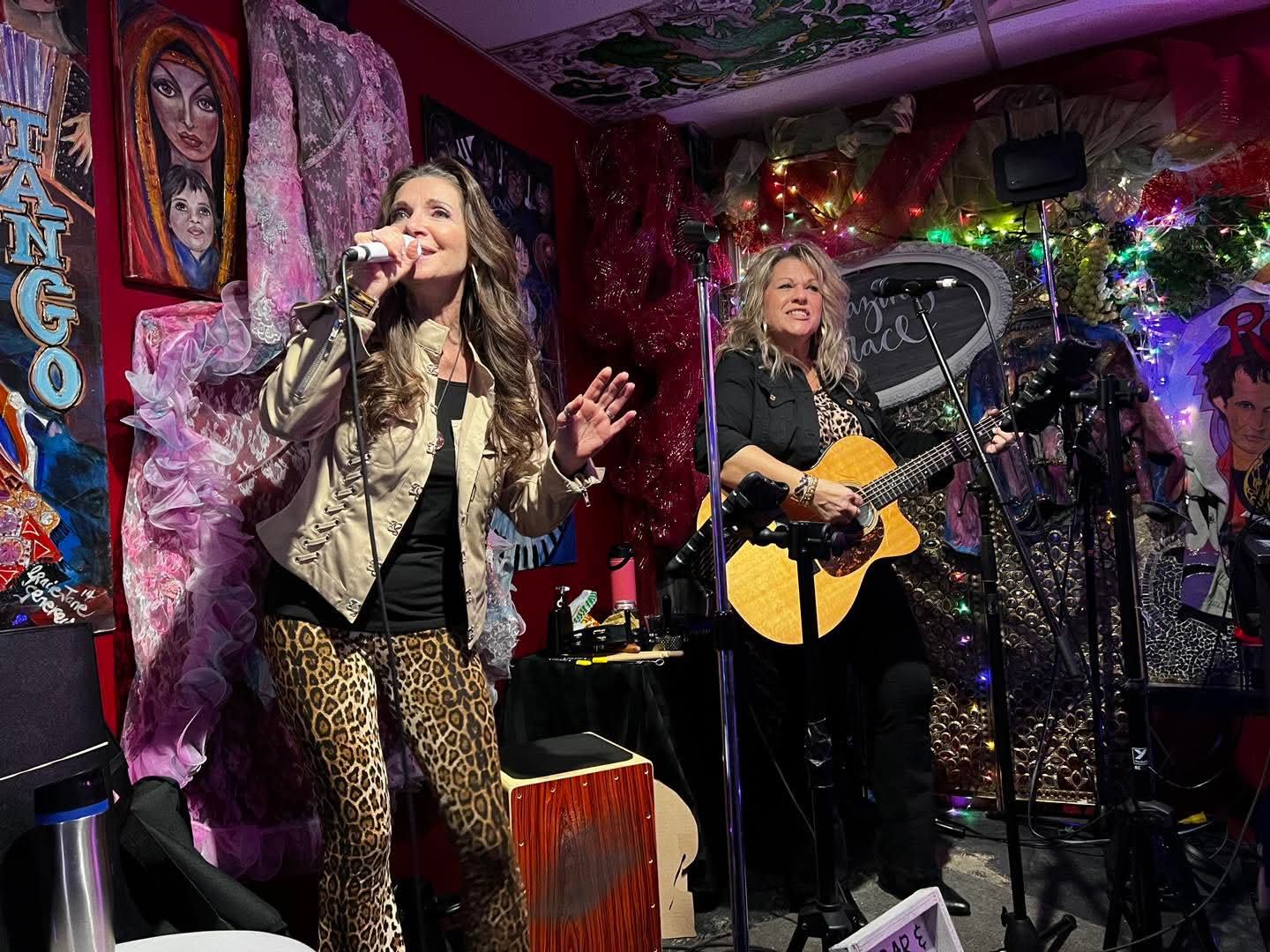 Singer and guitarist perform on a colourful stage surrounded by artwork and lights.