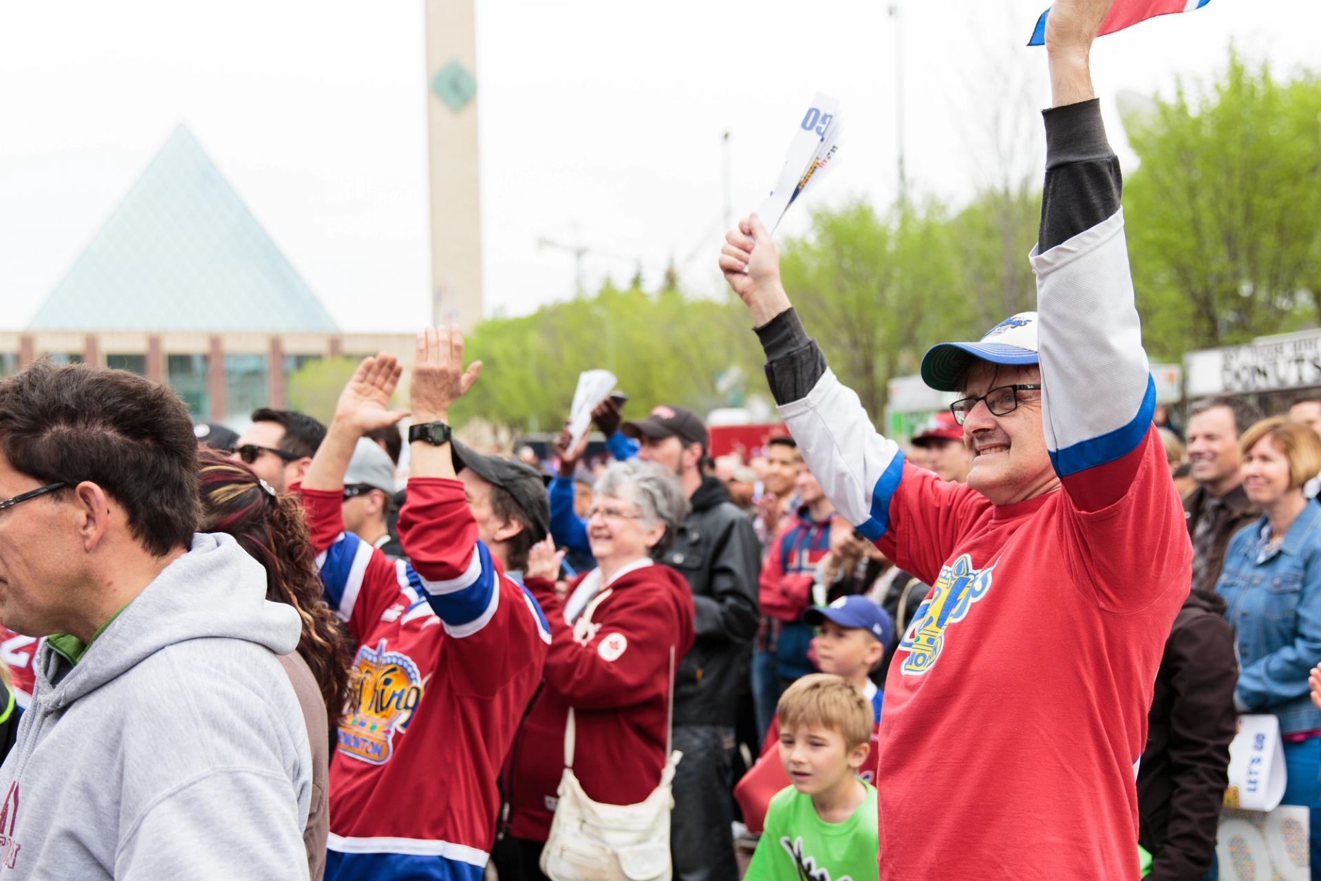 Fans in Edmonton Oil Kings jerseys cheer and hold hockey sticks at an outdoor event.