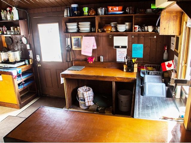 Rustic kitchen with wooden counters, shelves of dishes, and a small Canadian flag.
