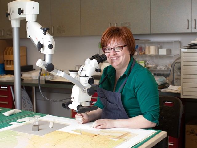 Person using microscope at Provincial Archives, engaged in document restoration in a research setting.