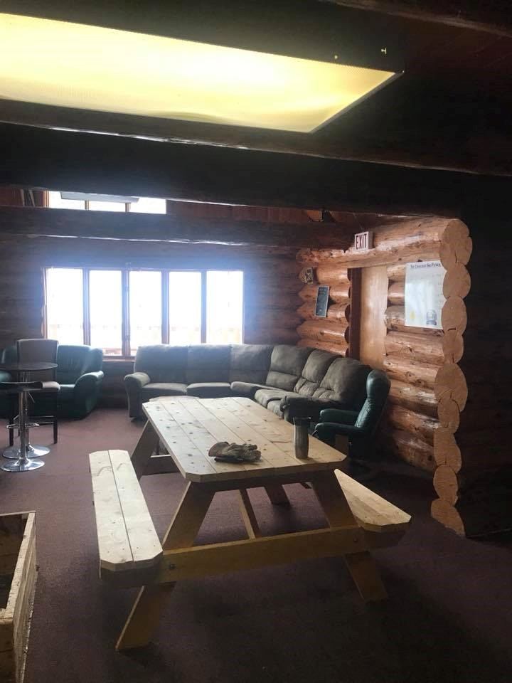 Wood-framed ski lodge lounge with sofas, chairs, and a rectangular wooden table near windows.