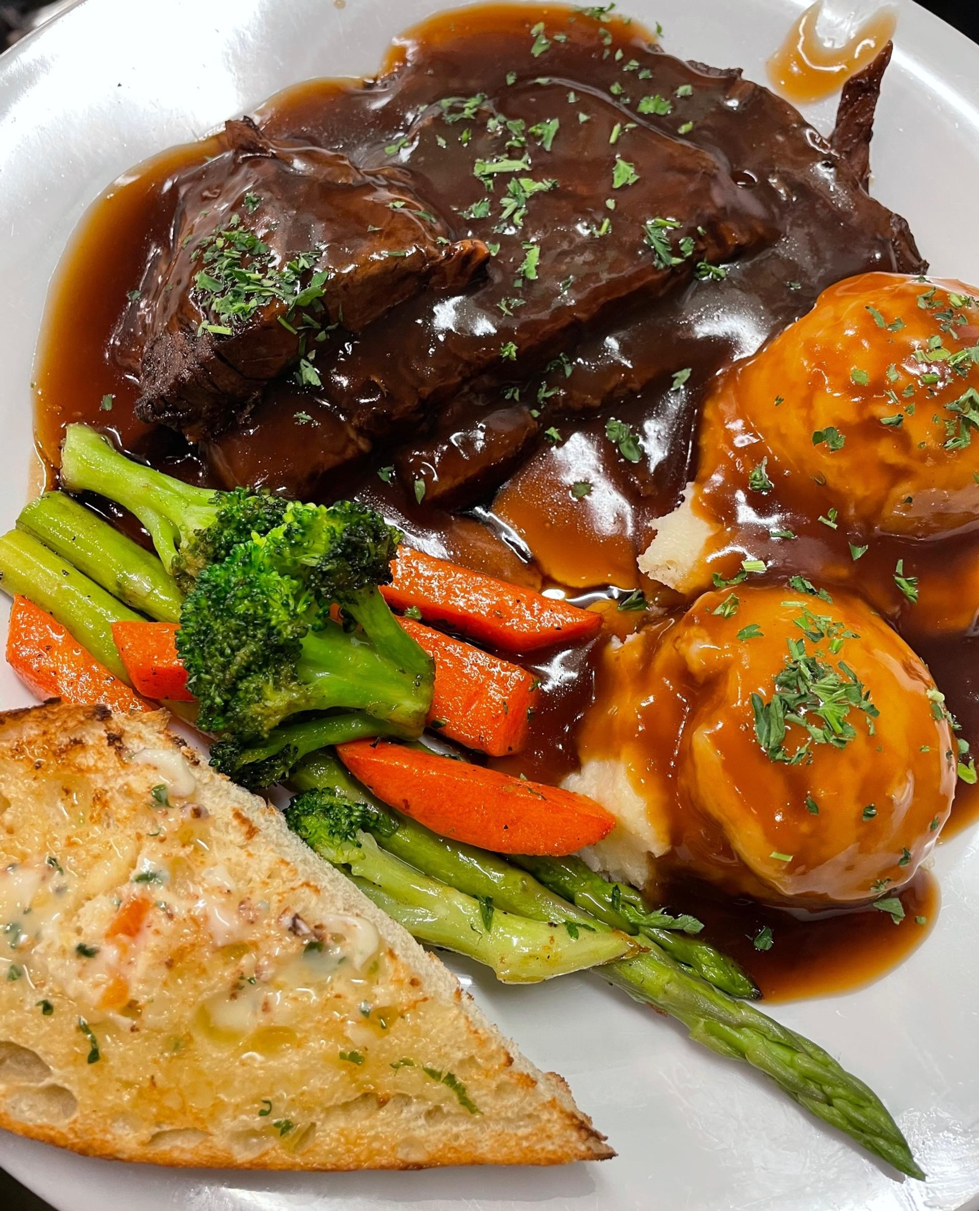 Roast beef with brown gravy, mashed potatoes, vegetables, and garlic toast