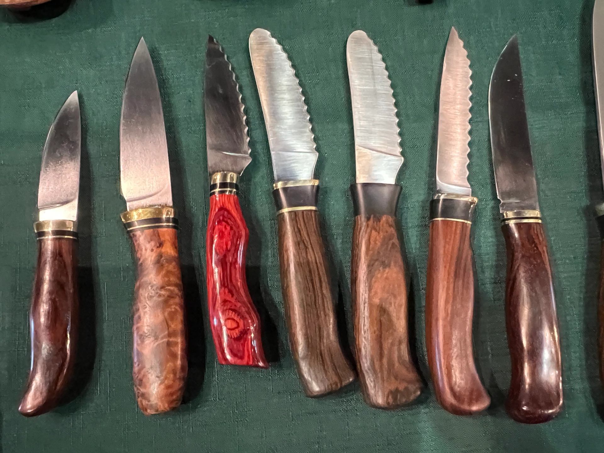 Assorted knives with wood handles displayed on green cloth.