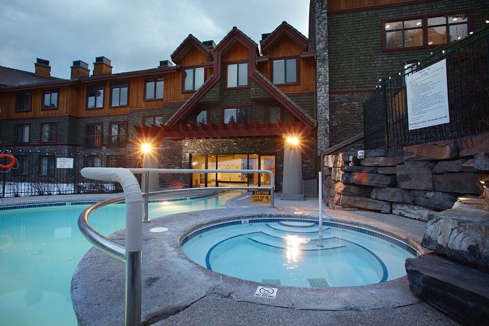 Heated pool and round hot tub near stone walls and resort building