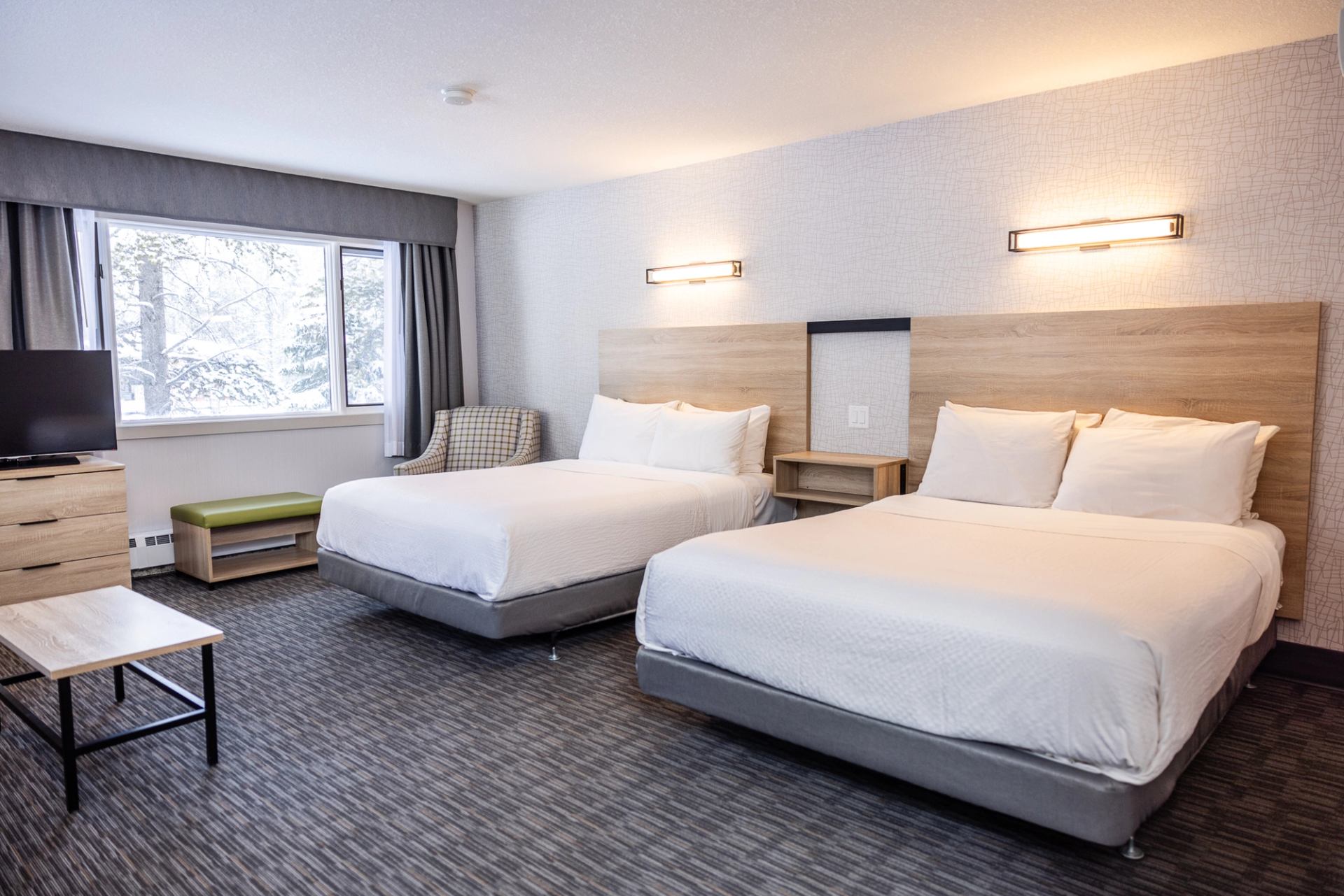 Modern hotel room at Mountaineer Lodge with two beds, TV, table, and window bench.