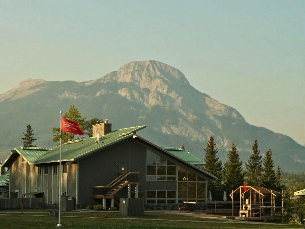 A building with a green roof and a red flag in front of a large mountain.