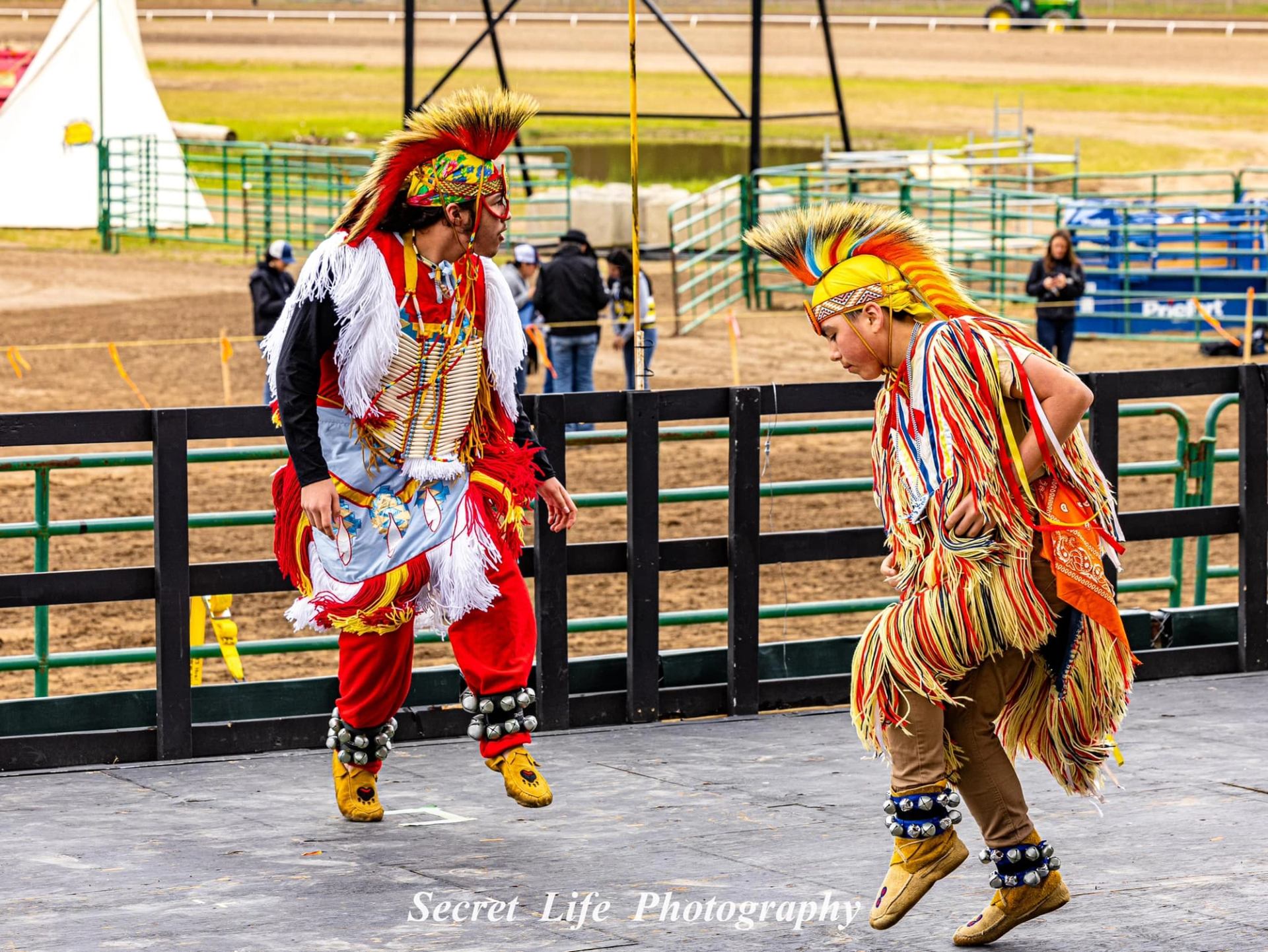 Two performers dancing in colorful regalia on an outdoor stage.