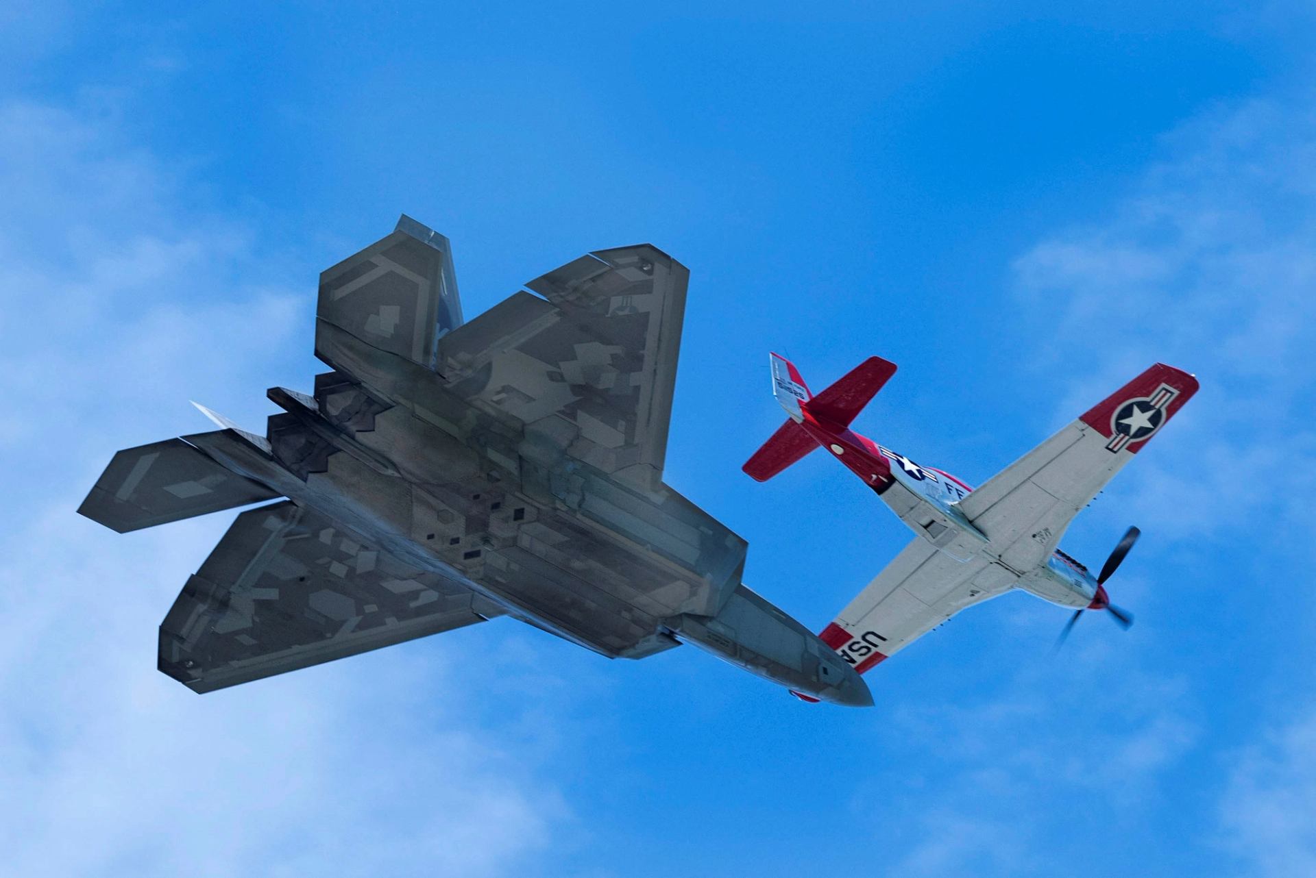 Modern fighter jet and vintage propeller plane flying side by side in clear sky.