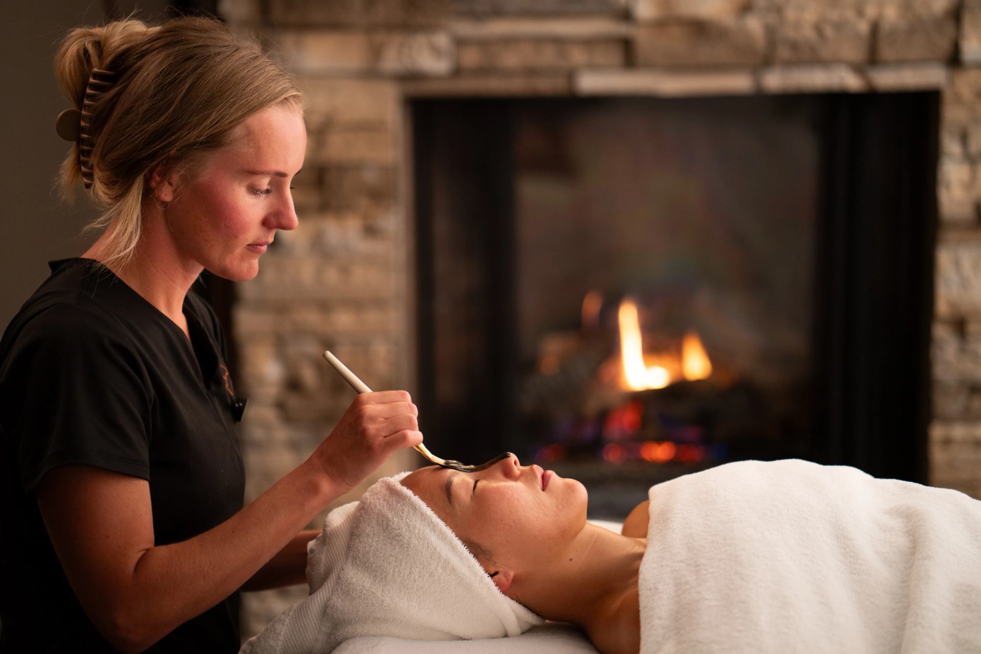 An esthetician providing a mud mask facial to a female guest. 
