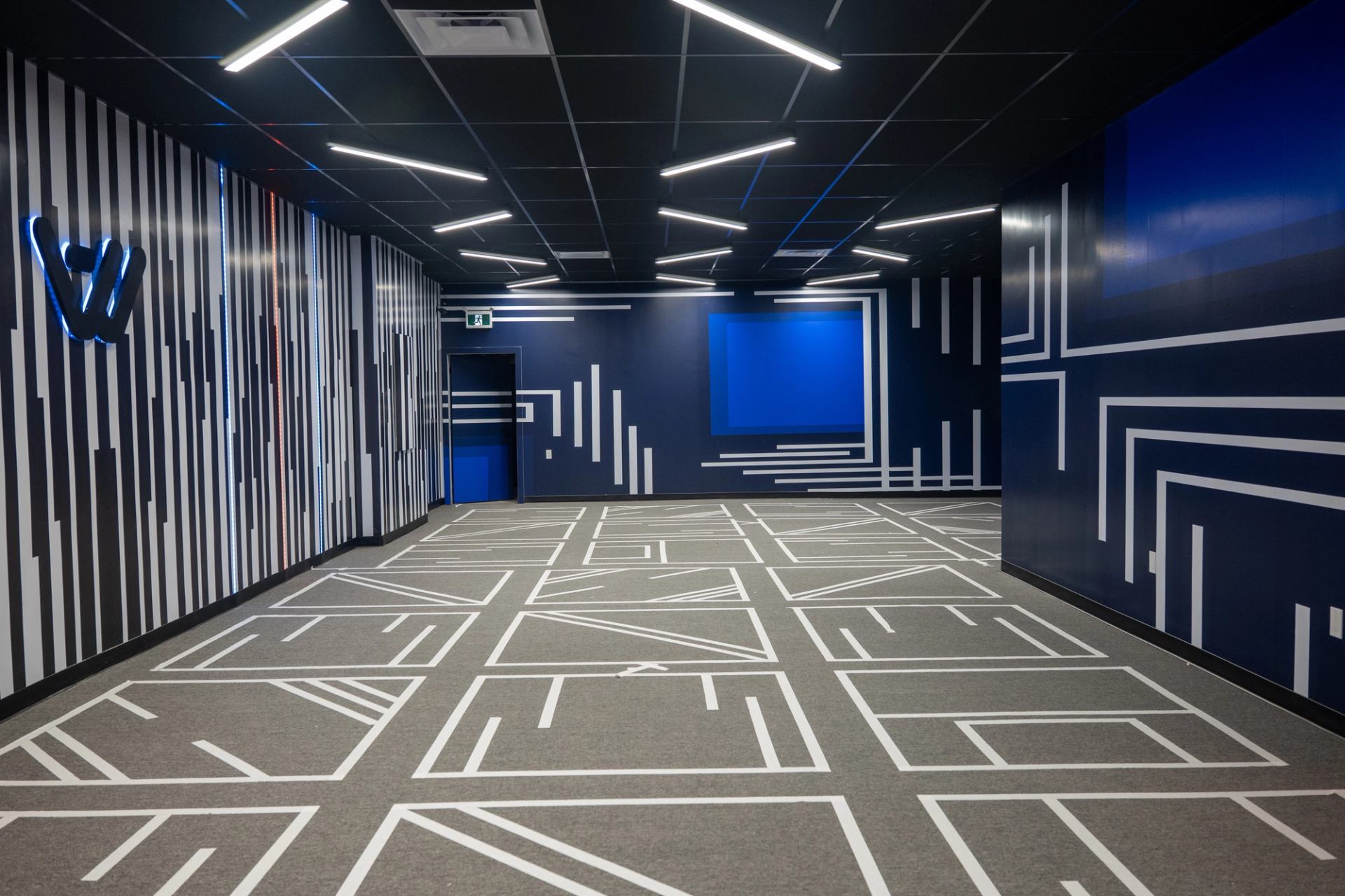 Empty corridor with geometric white lines across dark blue walls and grey carpet.