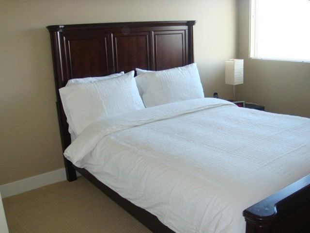 Neatly made bed with white linens and dark wooden headboard in a bright room.