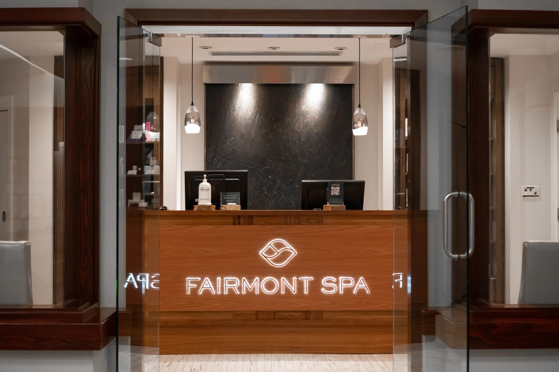 Fairmont Jasper Spa reception with wood desk, pendant lights, and glass doors.